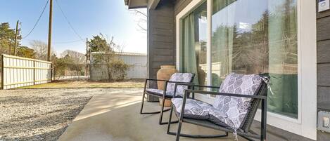 A patio with two rocking chairs, a concrete floor, and a large window with a view of trees and a fence.
