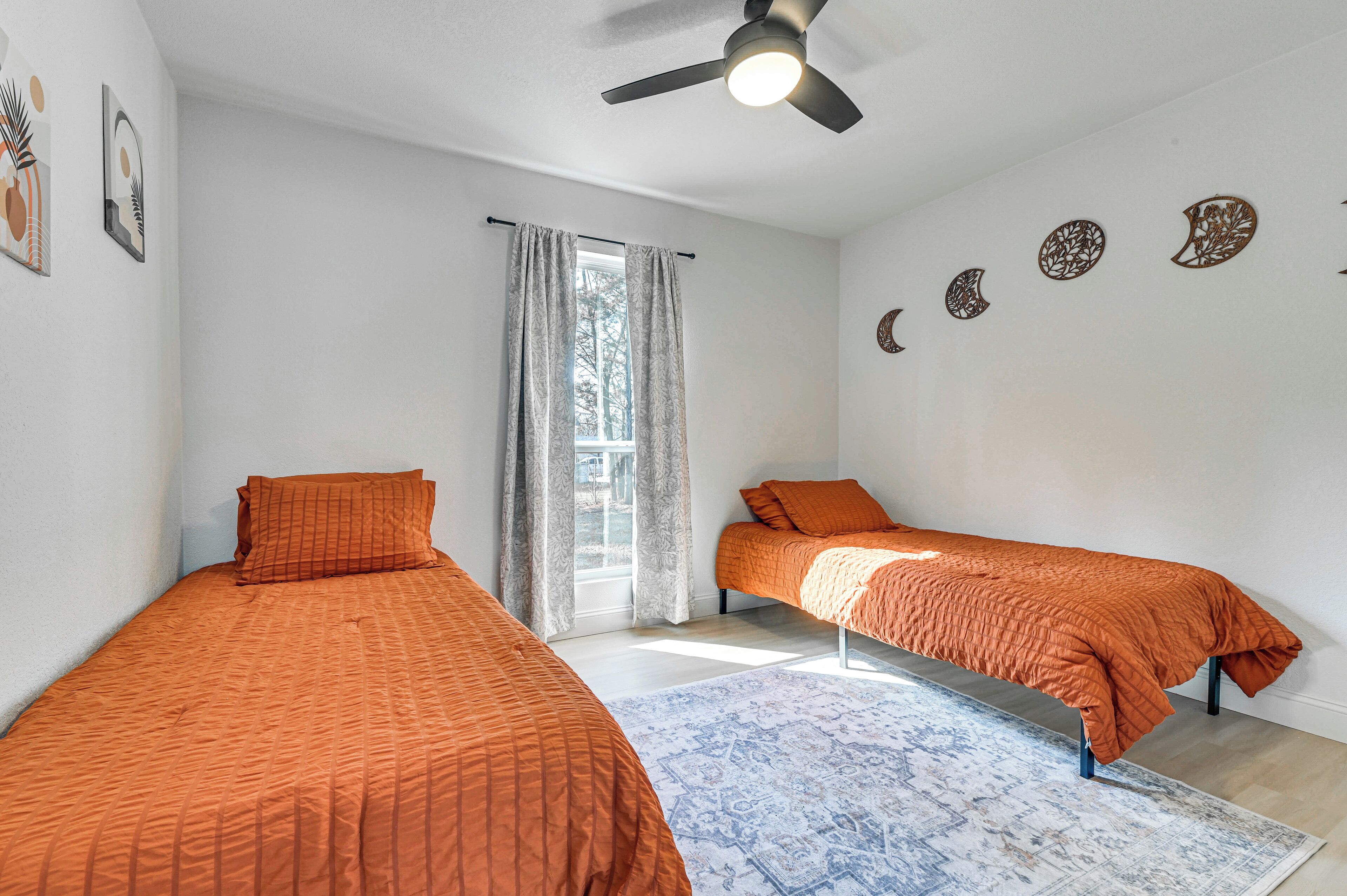 A room with two beds, a ceiling fan, a window with curtains, and wall decorations.