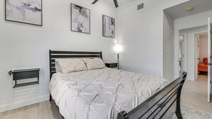 Un dormitorio con cama, ventilador de techo, decoración en la pared y mesita de noche.