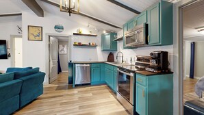 Een moderne keuken met blauwgroene kastjes, roestvrijstalen apparatuur en een houten vloer.