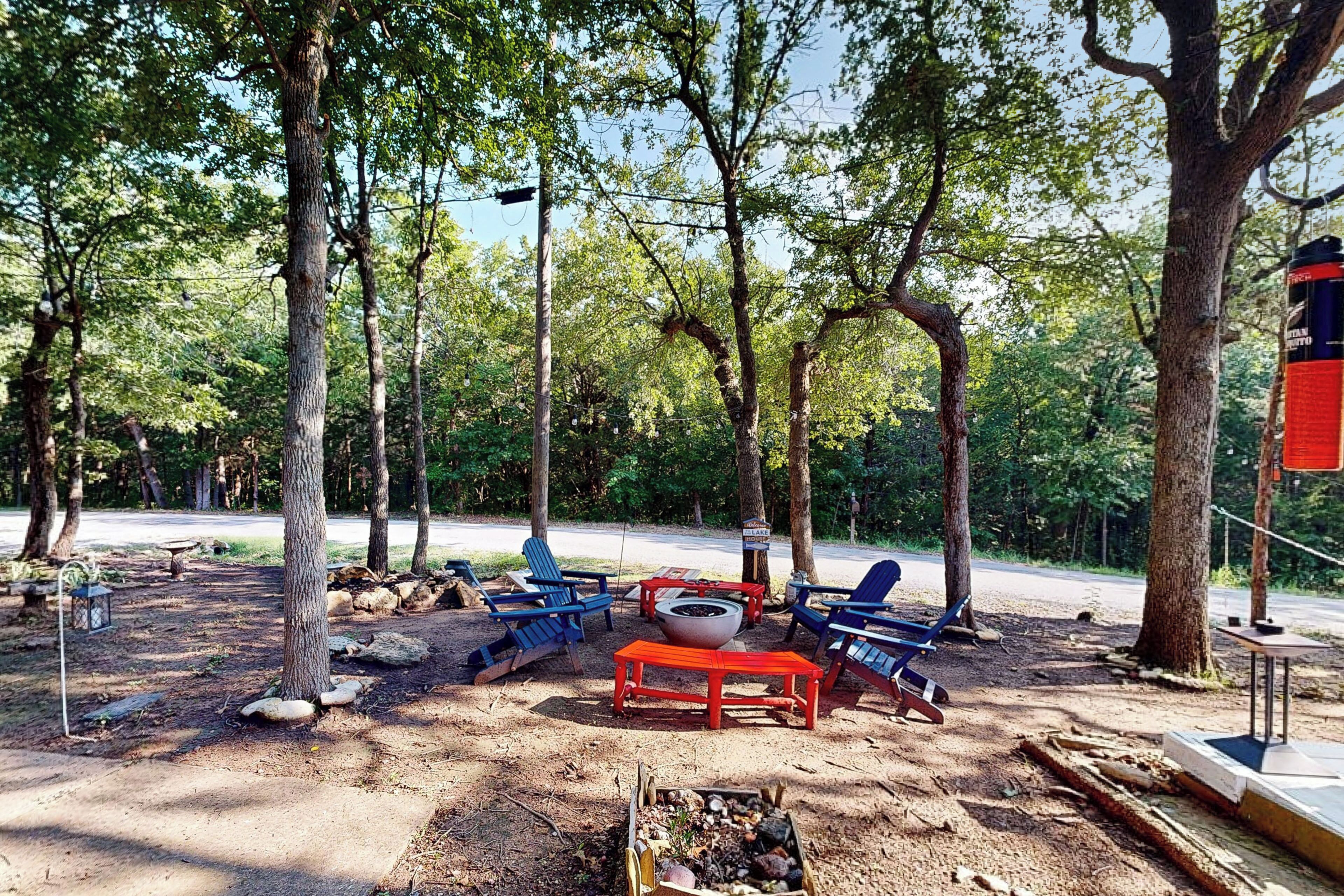 A campsite with a fire pit, red table, and blue chairs.