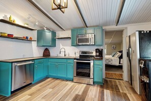 A modern kitchen with teal cabinets, stainless steel appliances, and wooden flooring. - Lake Texoma House w/ Golf Nearby! (Pottsboro)