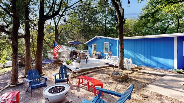 Een blauw huis met een terras, omringd door bomen en buitenmeubilair.