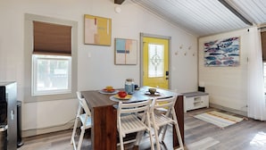 Een eetruimte met een houten tafel, witte stoelen, een gele deur en een muurschildering van vissen.