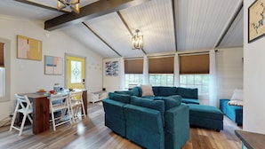 Een ruime woonkamer met een grote, blauwgroene hoekbank, houten vloeren en een eettafel met stoelen.
