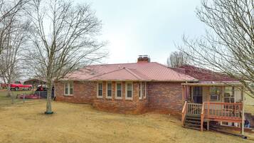 A brick house with a red roof, a porch, and a fenced yard.