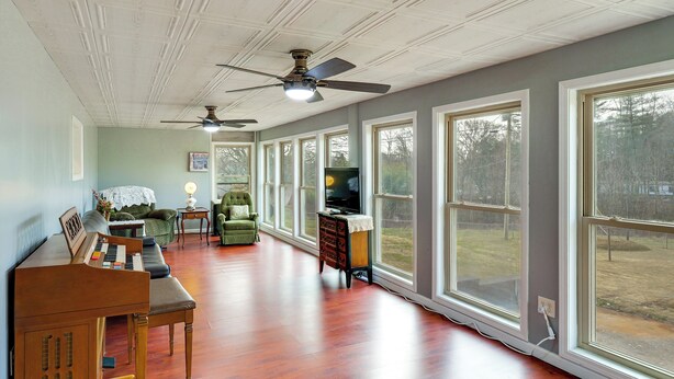 A spacious room with hardwood flooring, a piano, a green armchair, a television, and large windows.