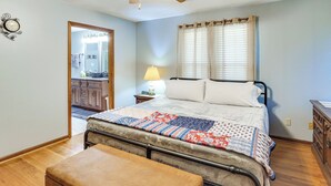 A bedroom with a bed, a nightstand, a lamp, a wooden bench, a ceiling fan, and a door leading to another room.