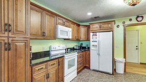 A kitchen with wooden cabinets, a white stove, a microwave, and a refrigerator.
