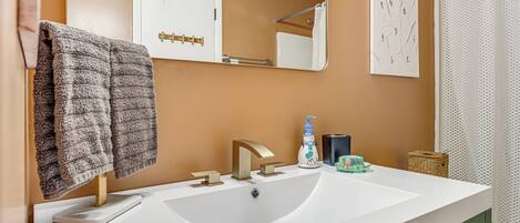 Un baño con lavamanos blanco, un espejo y un perchero para toallas.