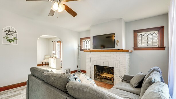 A living room with a gray sectional sofa, a white brick fireplace, a flat-screen TV mounted above the fireplace, and a ceiling fan. - 2 Mi to Syracuse University: Quiet Family Home (Syracuse)