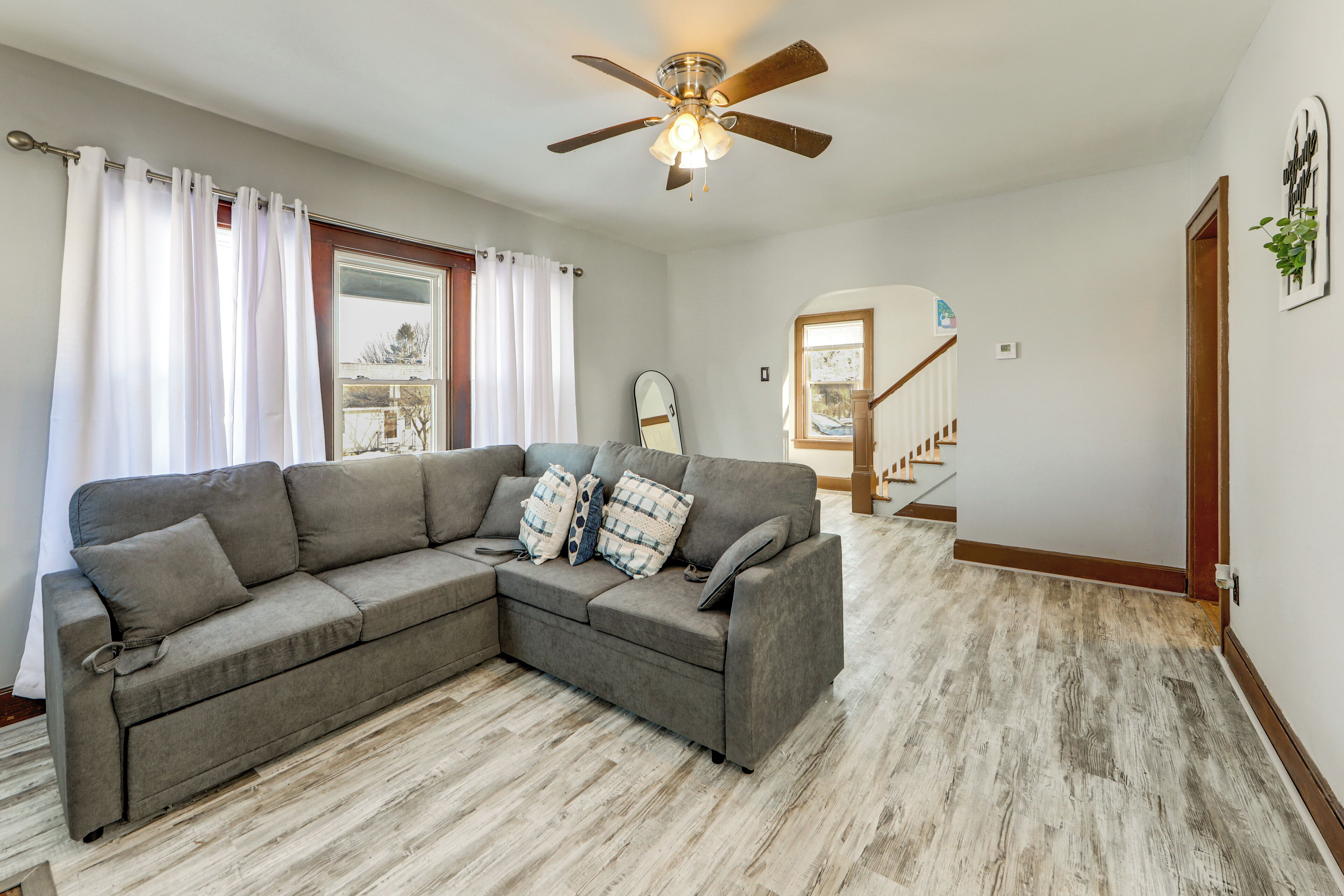 A living room with a sectional sofa, a ceiling fan, and a view of a staircase.