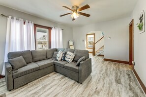 Una sala de estar con un sofá modular, un ventilador de techo y vista a una escalera.