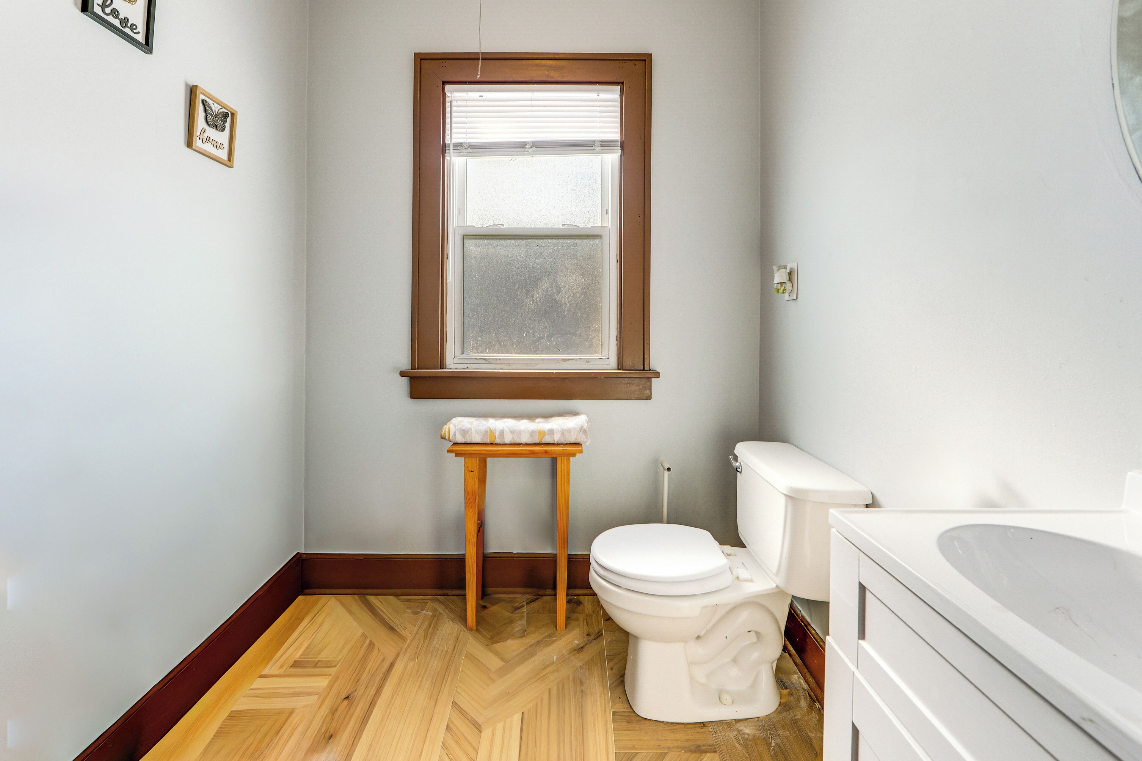 A bathroom with a wooden floor, a toilet, a sink, and a window with blinds.