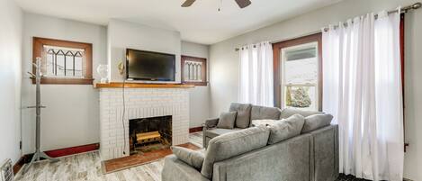 En stue med pejs, sofa, loftventilator og et tv ophængt på væggen.