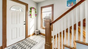 A hallway with a white door, a small round stool, a wooden staircase, and a framed picture on the wall. - 2 Mi to Syracuse University: Quiet Family Home (Syracuse)