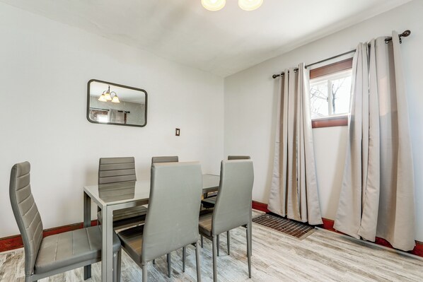 Un comedor con una mesa, cuatro sillas, un espejo y una ventana con cortinas.