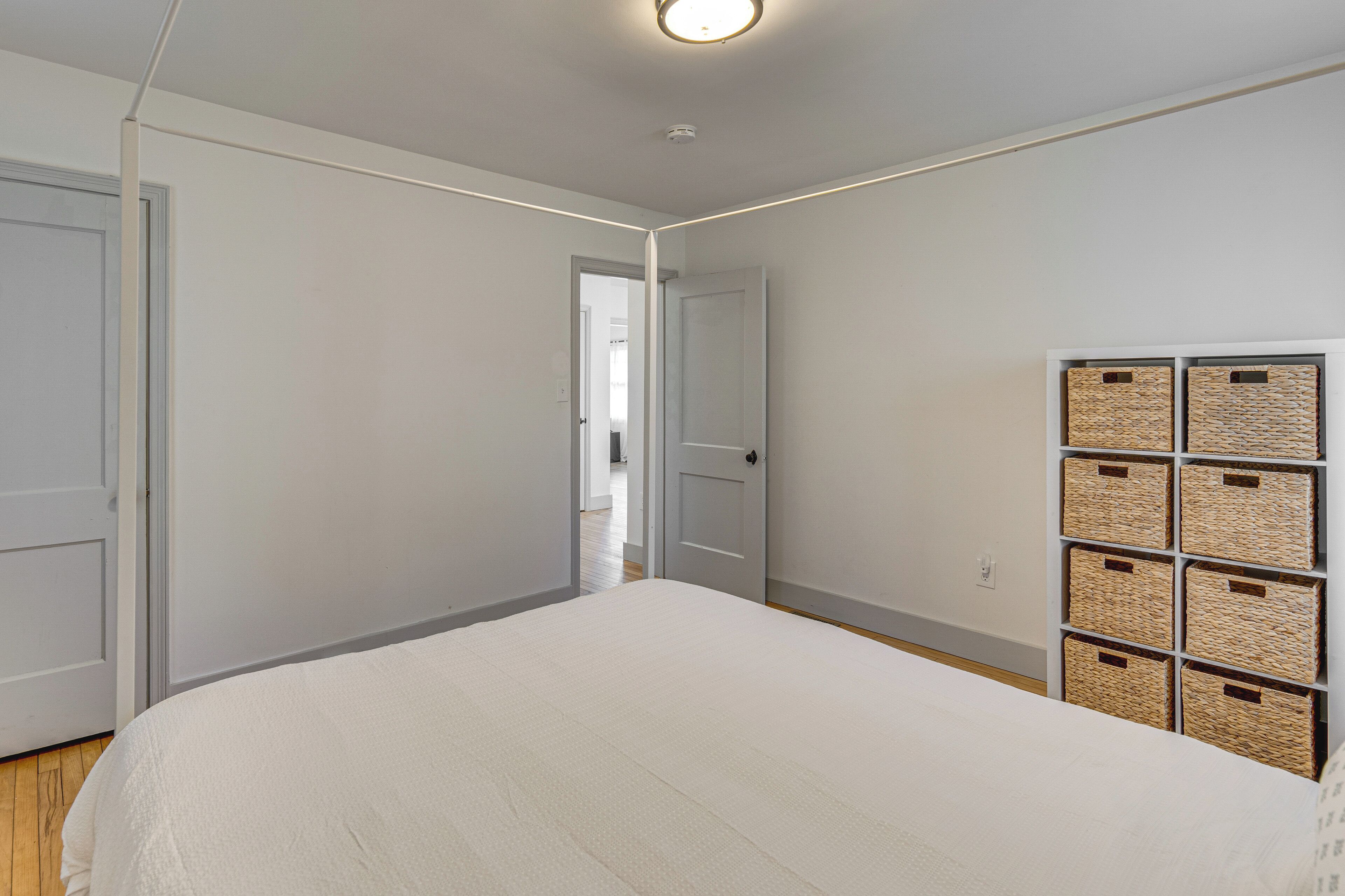Quarto com uma cama grande, um guarda-roupa com cestos e uma porta que dá para outro cômodo.