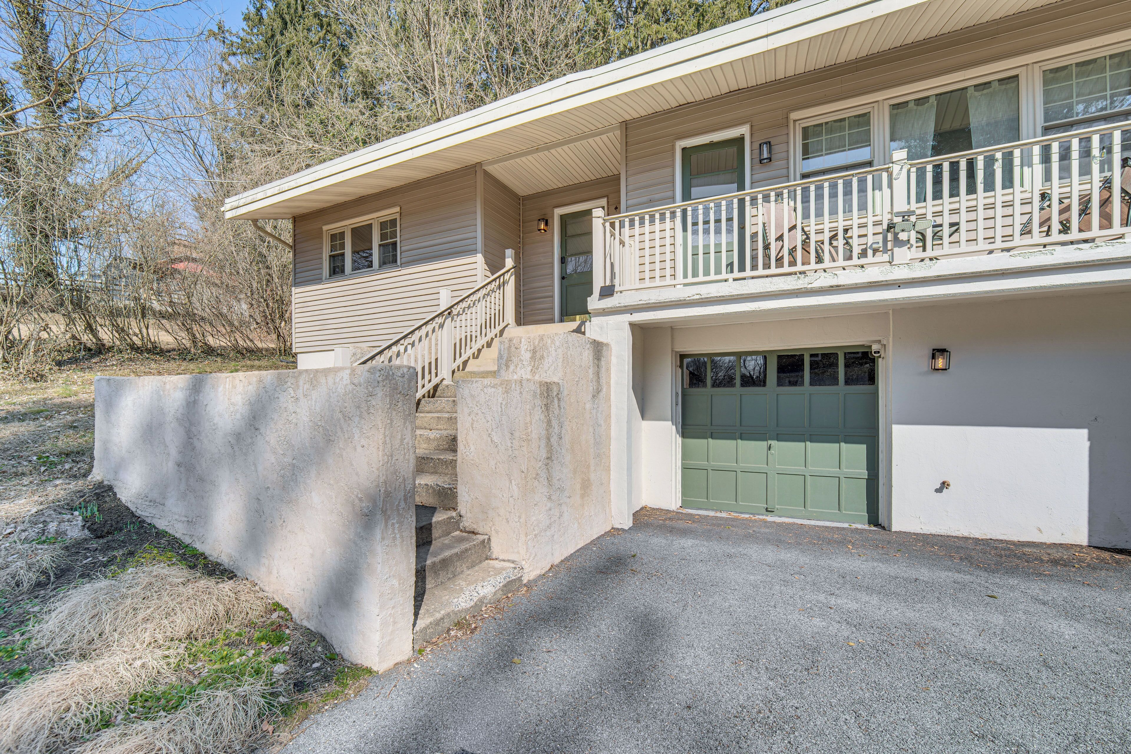Une maison à deux étages avec un porche à l’avant, une porte de garage verte et un escalier en béton menant à l’entrée.