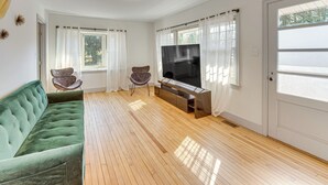 Un salón amplio con un sofá verde, un televisor de pantalla plana y dos sillones.