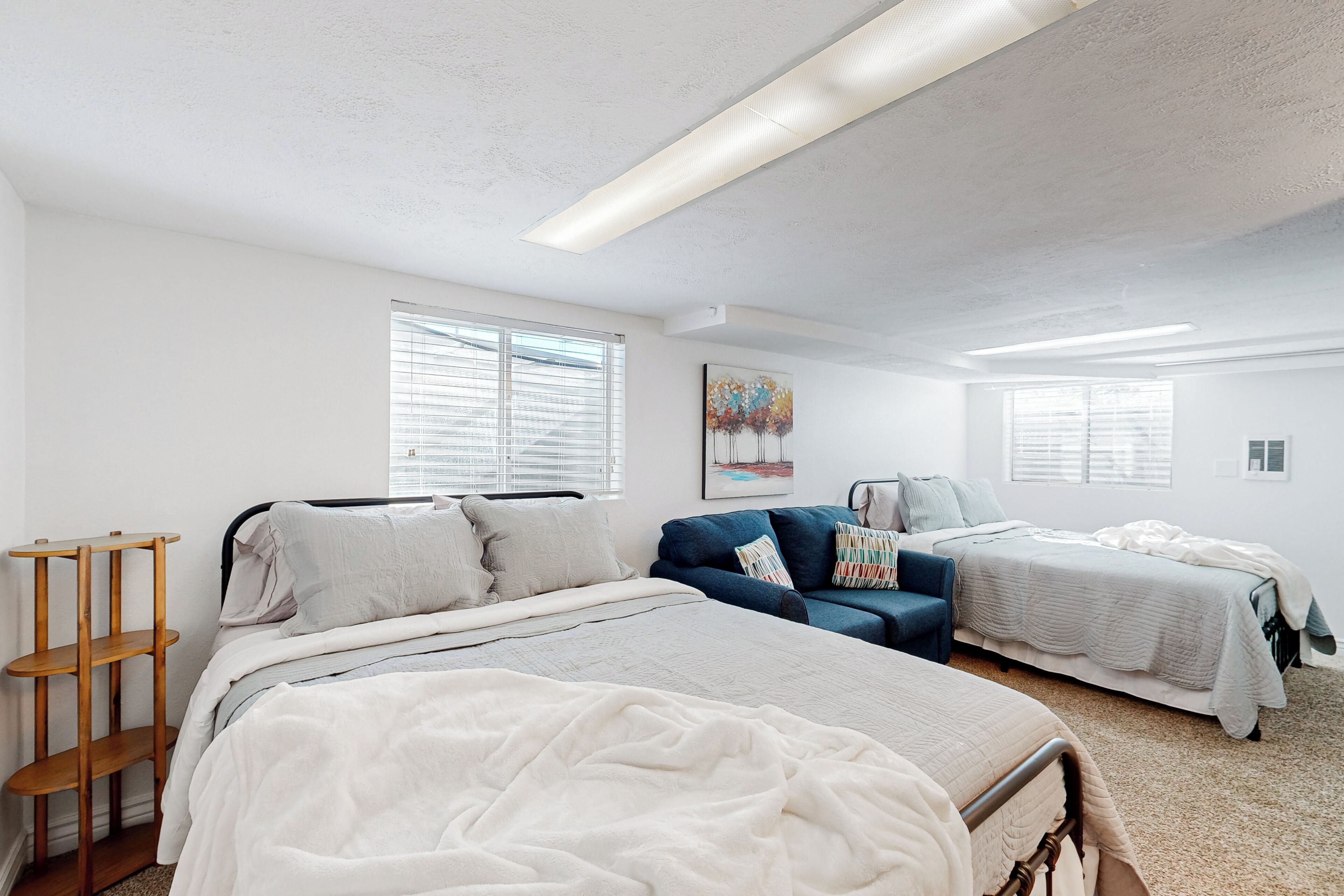 A bedroom with two beds, a blue sofa, and a wooden shelf.