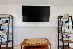 Una habitación con una mesa de madera que muestra una cuadrícula de objetos redondos, flanqueada por estanterías metálicas con diversos adornos.