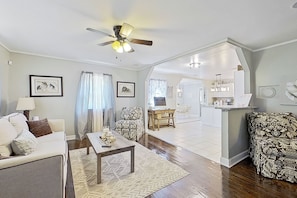 A spacious living room with a sofa, a coffee table, and a patterned armchair. A kitchen area is visible in the background with a dining table and chairs. - On-site Trails! 'serenity Acres Retreat' in Macon (Macon)