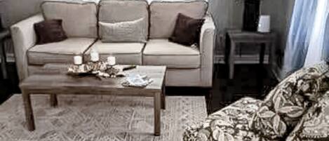 A living room with a sofa, a coffee table, and a patterned armchair.