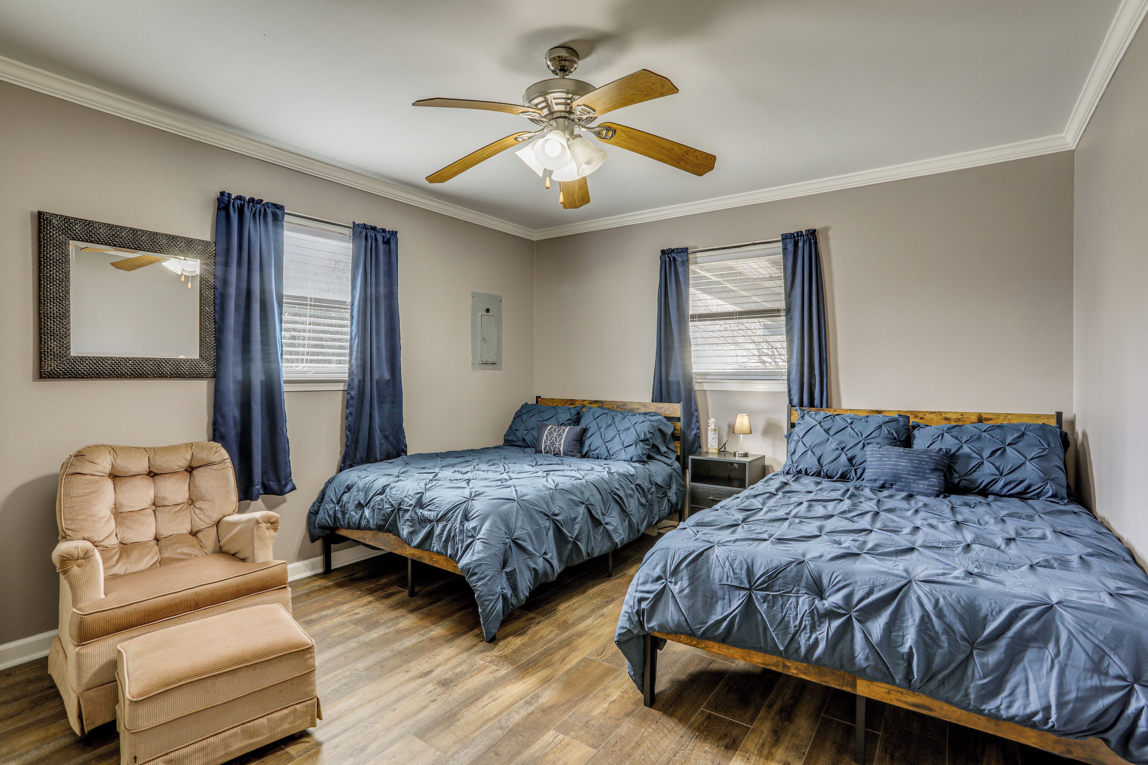 A bedroom with two beds, a chair, a ceiling fan, and a window with curtains.
