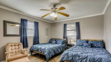 A bedroom with two beds, a chair, a ceiling fan, and a window with curtains.