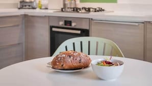 A kitchen with a loaf of bread on a plate and a bowl of salad on a table. - Peregrine Apartment Bowness (Bowness-on-Windermere)