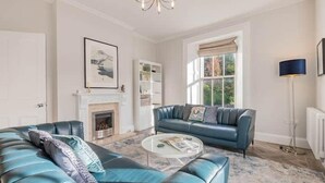 A spacious living room with a blue leather sofa, a round coffee table, and a fireplace. - Peregrine Apartment Bowness (Bowness-on-Windermere)