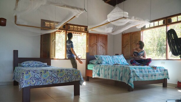 A room with two beds, a large window, and a ceiling fan.