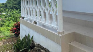 A white building with a balcony, a wooden window, and a view of greenery.