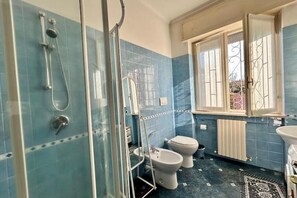 Une salle de bain avec une douche à parois de verre, deux toilettes, un lavabo et une fenêtre ornée de barreaux décoratifs.