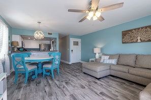 A modern living room with a dining area, a ceiling fan, and a kitchen in the background. - CNA1- Wow, Just Wow! Amazing View From Private Balcony! Kayaks Provided! (Gulf Shores)