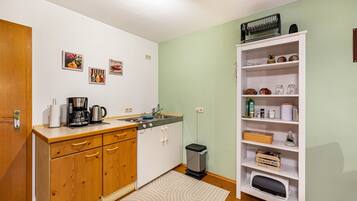Una cocina compacta con armarios de madera, una cafetera, un lavamanos y un cubo de basura.