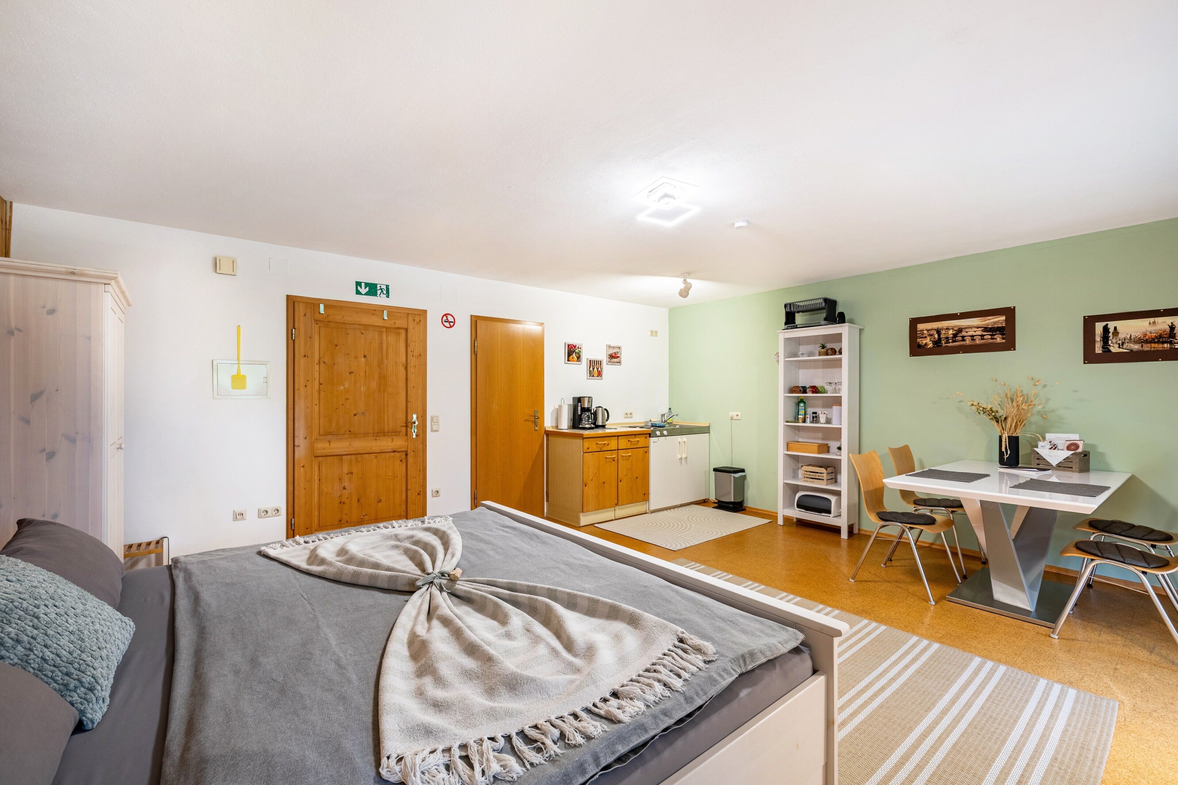 Una habitación con cama, escritorio, silla, estantería y mesa de comedor.
