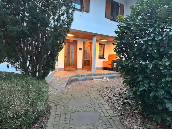 A building with a stone pathway leading to a wooden door, surrounded by greenery.
