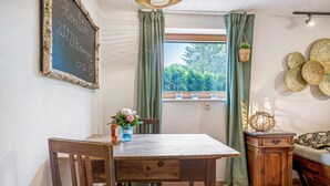 Un coin repas comprenant une table en bois, des chaises, un tableau noir avec du texte, une fenêtre avec des rideaux et des œuvres d’art décoratives accrochées au mur.
