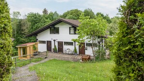 Une maison à deux étages avec une terrasse en bois, un petit abri de jardin et un jardin.