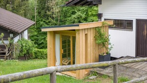 Une structure en bois dotée d’une porte et d’une petite fenêtre, entourée de verdure.