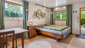 Une chambre à coucher avec un lit en bois, une petite table, une chaise, une fenêtre avec des rideaux et des éléments de décoration murale.
