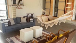 Un salon avec un canapé, deux poufs, un hamac et un tapis à motifs.