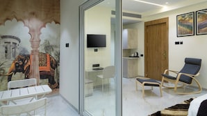 Une chambre moderne avec une cloison en verre, une fresque représentant un éléphant, un bureau, une chaise, un lit, un téléviseur et une porte en bois.