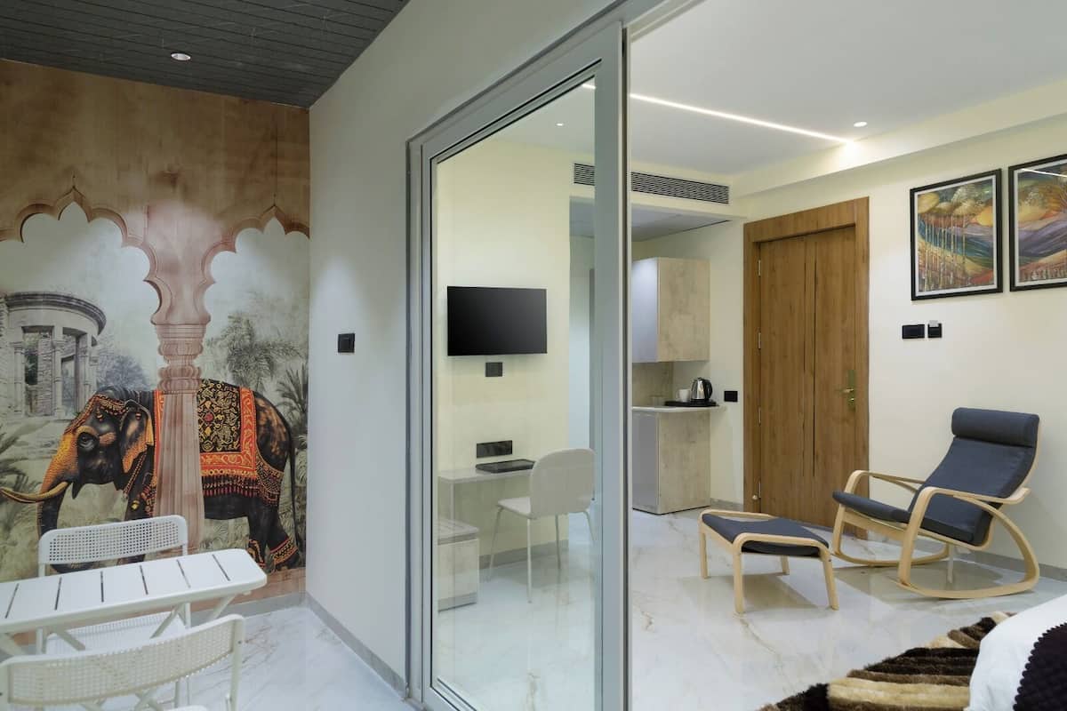 A modern room with a glass partition, a mural of an elephant, a desk, a chair, a bed, a TV, and a wooden door.