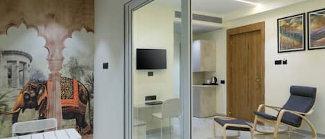 A modern room with a glass partition, a mural of an elephant, a desk, a chair, a bed, a TV, and a wooden door.