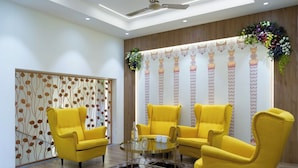 Un salon moderne avec des fauteuils jaunes, une table basse en verre et un mur décoratif orné de motifs verticaux.