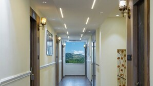 Un long couloir bien éclairé, doté d’un plancher en bois, avec des portes de chaque côté, et offrant une vue sur un paysage montagneux par les fenêtres au bout.