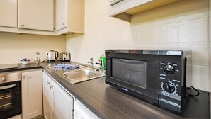 Una cocina con gabinetes blancos, un lavamanos de acero inoxidable, un microondas negro y un tostador.